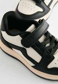 Sort og creme sneakers med lædermateriale, mesh-indlæg, rund tå, snørebånd og velcro-lukning samt gummisål.