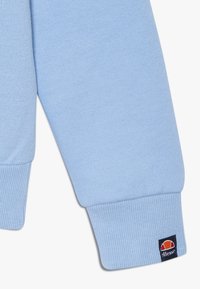 Manga de sudadera azul clara, hecha de tejido suave, con puños de canalé y un pequeño parche con el logo de la marca cerca del dobladillo.