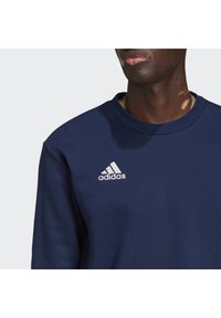 Felpa blu navy in cotone con colletto tondo. Presenta un piccolo logo bianco di Adidas nella parte superiore sinistra del petto.