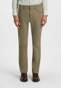 Chinos beige avec une coupe droite, fabriqués en tissu lisse. Comprend deux poches avant, une fermeture à bouton et se porte avec des chaussures marron.