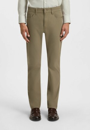 Beige chinos with a straight fit, made from smooth fabric. Features two front pockets, a button closure, and is worn with brown shoes.