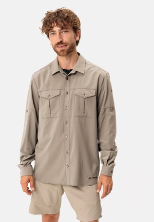 Chemise beige légère à manches longues avec deux poches avant, fermetures à boutons et un logo en bas. Tissu doux au toucher lisse.
