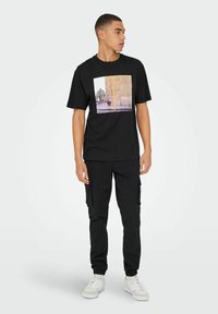 Camiseta negra de cuello redondo con un estampado gráfico colorido de un diseño floral. Combinada con pantalones cargo negros y zapatillas blancas.