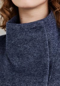 Dark blue high-collared garment made of textured fabric. Close-up reveals a smooth, structured design with a refined finish.