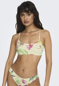 Ensemble de bikini floral avec une base jaune ornée de motifs roses et verts. Le haut a des fines bretelles et un design court ; le bas a une coupe haute.