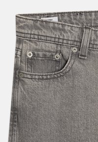 Hallid teksapüksid, millel on tekstuuriga kangas, eesmine tasku hõbedaste detailidega ja nähtavad õmblused vööjoonel.