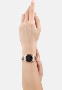 Roségoldene Uhr mit schwarzem Zifferblatt, rundem Gehäuse und gliedertem Armband. Verfügt über einfache Stundenmarkierungen und eine Datumsanzeige auf 3 Uhr.