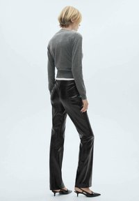 Grijze cropped trui gecombineerd met glanzende zwarte broeken; de outfit heeft een strakke pasvorm en een soepele textuur, aangevuld met puntige schoenen.