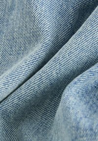 Jasnoniebieska tkanina dżinsowa o gładkiej fakturze, diagonalnym wzorze splotu i miękkich fałdach, ukazująca subtelne różnice w odcieniu.