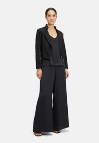 Zwart suède cropped jack met een ritssluiting, gecombineerd met een donkere tanktop en wijde broekspijpen. Zachte stof en een relaxte pasvorm.