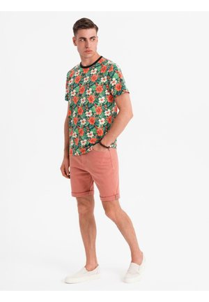 Korte mouwen bloemen T-shirt met groene, oranje en witte patronen, gecombineerd met roze shorts en witte instappers. Schone, casual uitstraling.