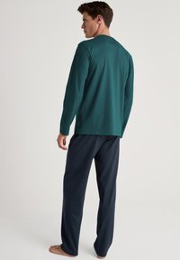 Langsleeve oceaanblauw shirt met een ronde hals, gecombineerd met donkerblauwe broek. De stof lijkt zacht en lichtgewicht, met minimale details.