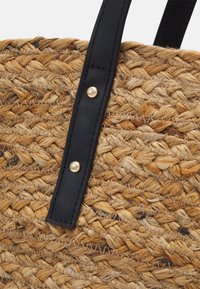 Woven straw bag with a natural tan color, featuring a black leather handle with gold hardware accents for durability and contrast.