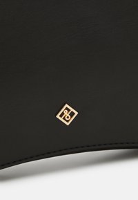 Surface en cuir noir avec un petit logo carré doré présentant un motif abstrait bouclé au centre.