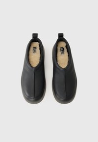 Fekete bőr slip-on cipők, puha szőrmével bélelve, minimális dizájnnal és lekerekített orral. Méretcímkék láthatók a belsejében.