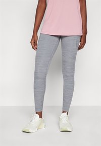 Leggings gris ajustados con una textura jaspeada, combinados con una camiseta de manga corta rosa y zapatillas deportivas blancas.