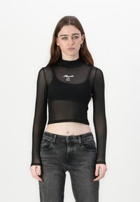 Black long-sleeve cropped top in sheer mesh with high neck; features white embroidered text "Thanks OK Bye." Paired with faded black jeans.