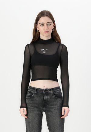 Black long-sleeve cropped top in sheer mesh with high neck; features white embroidered text "Thanks OK Bye." Paired with faded black jeans.