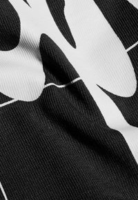 Svart tyg med en strukturerad väv som har stora vita abstrakta mönster. Ytan verkar något rynkad och mjuk.