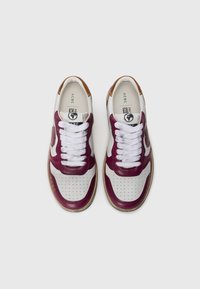 Sneaker bordeaux e bianche con texture perforata, lacci bianchi e dettagli marroni sul tallone e sulla linguetta. Suola piatta in gomma.