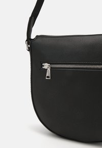Borsa a tracolla in pelle nera con superfice testurizzata, forma curva e dettagli in zip color argento sulla tasca anteriore.
