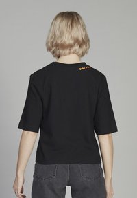 Camiseta de algodón negra con mangas cortas, que presenta el texto naranja "Talk it Out" en la parte posterior del cuello. Diseño simple y de corte relajado.