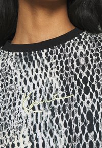 Czarny i biały wzorzysty t-shirt z krótkim rękawem z nadrukiem węża i lekkiego materiału. Haftowane logo w jasnym żółtym kolorze.