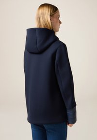 Felpa con cappuccio blu navy caratterizzata da una trama liscia, con una vestibilità morbida e polsini imbottiti a contrasto. Design semplice senza ulteriori motivi.