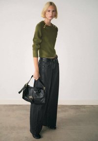 Maglione a maglia verde oliva con bottoni sulle spalle, abbinato a jeans neri a gamba larga con vita alta e una borsa in pelle nera con dettagli dorati.