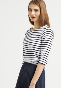 Stribet shirt med marineblå og hvide vandrette striber, scoop neckline, 3/4-langærmet, parret med en plisseret marineblå nederdel.