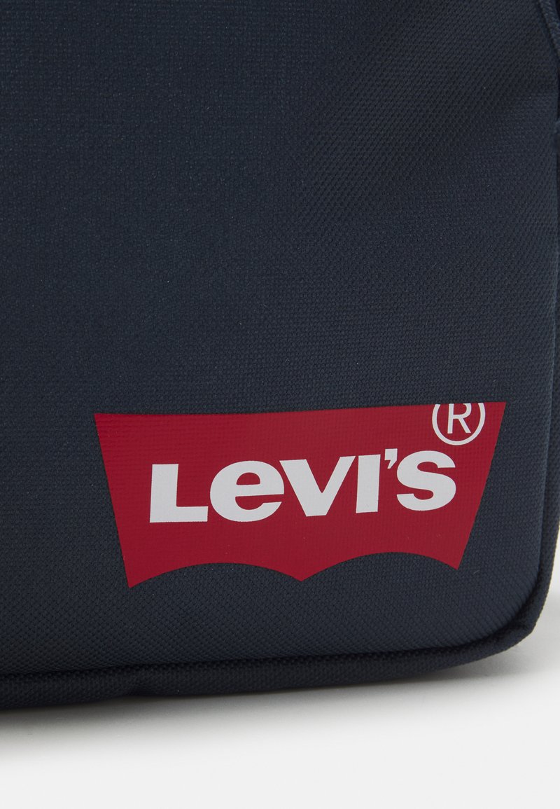 Sac en tissu bleu marine avec un grand logo rouge de Levi's et du texte blanc. Présente une surface texturée et une forme de logo arrondie sur un fond rectangulaire.