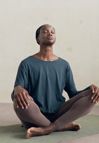 Osoba sjedi prekriženih nogu na joga prostirci s zatvorenim očima, rukama oslonjenim na koljenima, prakticirajući meditaciju ili svjesnost unutra.