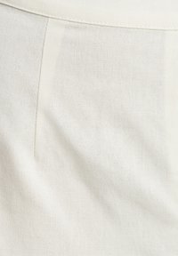 Biały materiał o subtelnej teksturze, z gładką, czystą powierzchnią i drobnym, starannie przeszytym detalem szwu.