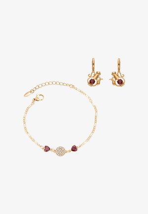 Złota bransoletka z sercowymi czerwonymi kamieniami i zawieszką w kształcie uśmiechniętej buźki, w zestawie ze złotymi kolczykami z czerwonymi kamieniami.