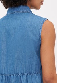 Αμάνικο μπλε τζιν φόρεμα με γιακά, συγκεντρωμένη μέση και απαλή υφή, που επιδεικνύει έναν κλασικό casual σχεδιασμό.