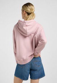 Lichtroze sweatshirt met capuchon, een relaxte pasvorm, zachte textuur en geribbelde manchetten. Gecombineerd met blauwe denim shorts, zichtbaar ontwerp van de achterzak.