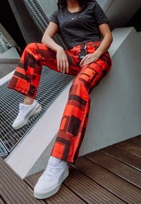 Röda och svarta mönstrade vida byxor i kombination med en svart atletisk t-shirt och vita sneakers. Designen har geometriska former.