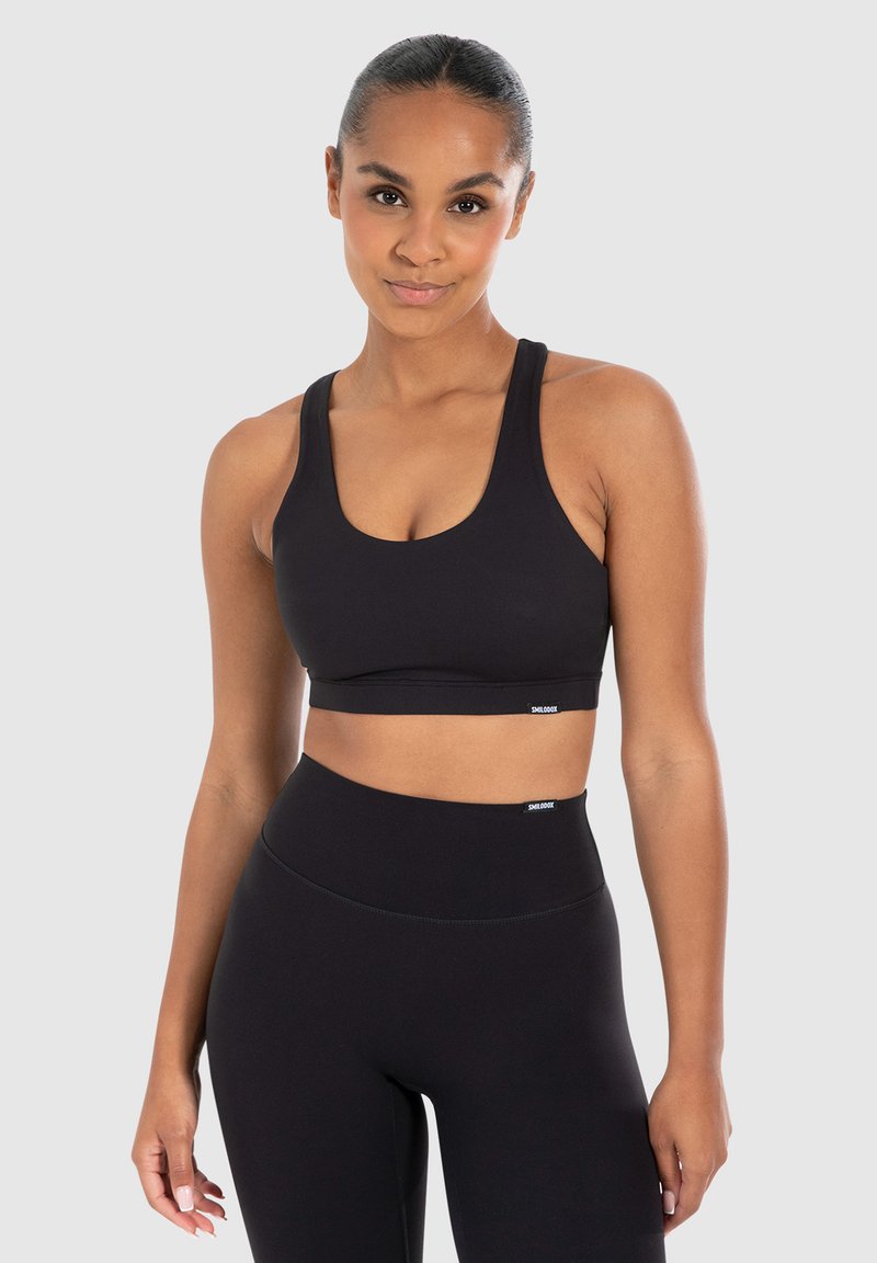 Zwarte sport-bh met brede banden en een ronde hals. Materiaal lijkt rekbaar. Draagt in combinatie met bijpassende hoge zwarte leggings, minimale merknaam.