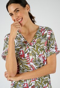 Camisa de manga corta con un patrón floral que presenta plantas rojas y verdes sobre un fondo blanco, escote en V y detalle de botones en la parte delantera.