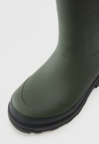 Botte en caoutchouc verte avec une surface texturée, bout rond et semelle noire. Matériau lisse avec un léger éclat ; conçue pour être résistante à l'eau.