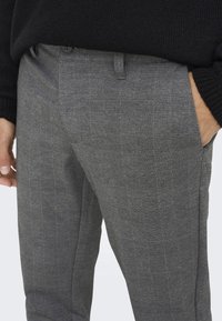 Grijze geplaid broek gemaakt van een gestructureerde stof, met zijzakken en een knoopsluiting.