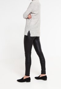 Světle šedý pletený svetr se bočními rozparky, zkombinovaný s černými kalhotami z umělé kůže s žebrovanými detaily a černými semišovými slip-on botami.