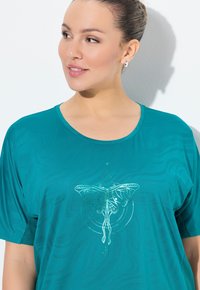 Camiseta de manga corta en color azul verdoso, hecha de un tejido ligero, que presenta un gráfico de mariposa blanca en el centro. Diseño con escote redondo y corte relajado.