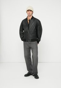 Melna ādas bombjera jaka ar rievotiem manžetēm, rāvējslēdzēja aizdari un sānu kabatu. Valkāta kopā ar pelēniem džinsiem un krēmkrāsas adītu cepuri.