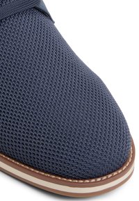 Parte superior de zapato de malla en color azul marino con una superficie texturizada, suela en tono marrón claro que contrasta y punta redondeada. Presenta un acento suave a lo largo del empeine.