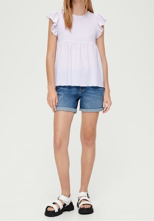 Blusa viola chiara con maniche a frill, corpetto arricciato. Abbinata a pantaloni corti in jeans con risvolti. Le scarpe sono sandali bianchi con piattaforma e cinturini.