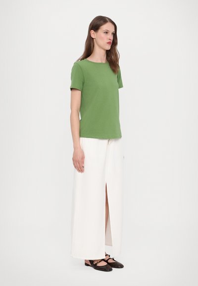 Πράσινο κοντομάνικο μπλουζάκι από βαμβάκι, συνδυασμένο με κρεμ παντελόνι σε φαρδιά γραμμή με άνοιγμα στο μπροστινό μέρος. Καφέ flat παπούτσια ολοκληρώνουν την εμφάνιση.