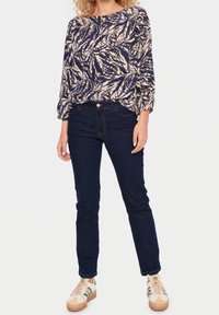 Bluzka z długim rękawem w granatowy i kremowy wzór liści; zestawiona z ciemnoniebieskimi dżinsami; model nosi jasne sneakersy z zielonymi akcentami.