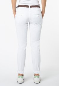 Witte denim broek met een slim fit, voorzien van achterzakken, opgerolde mouwen en een gevlochten bruine riem. Gecombineerd met witte sneakers met groene accenten.