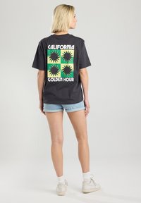 Harmaa lyhythihainen t-paita, jossa on takapuolella keltainen ja vihreä neliökuvio sekä teksti "CALIFORNIA GOLDEN HOUR". Yhdistetty farkkushortsien kanssa.